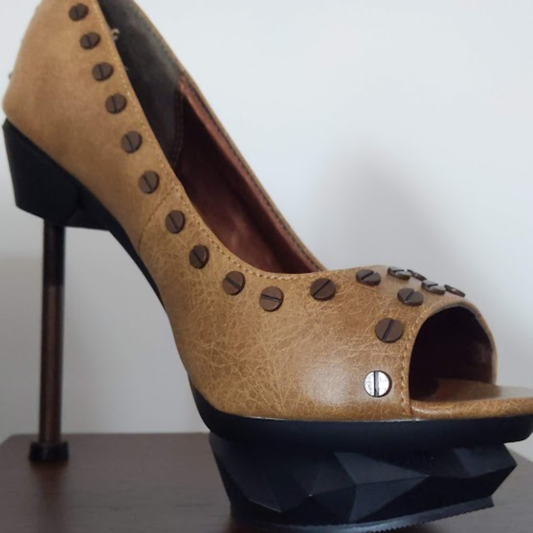 Mustard coloured high heeled open toed shoe with an interestding black geometric platform an industrial bolt for a heel decorated with rivets.
