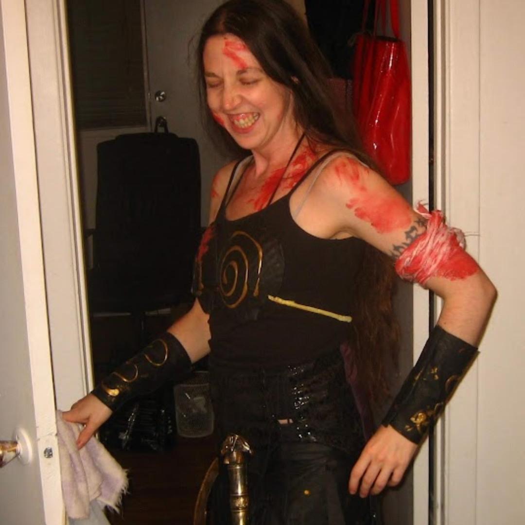 A white woman in a Xena Warrior Princess costume.  She is covered in fake blood and laughing.