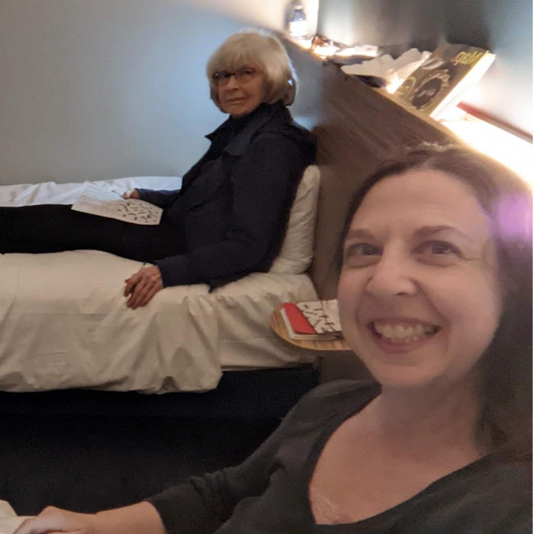 A mother and daughter sitting on side by side twin beds in a hotel room.